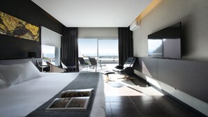 Een moderne hotelkamer met een groot bed, een flatscreen televisie, een zithoek met stoelen en uitzicht op de skyline.