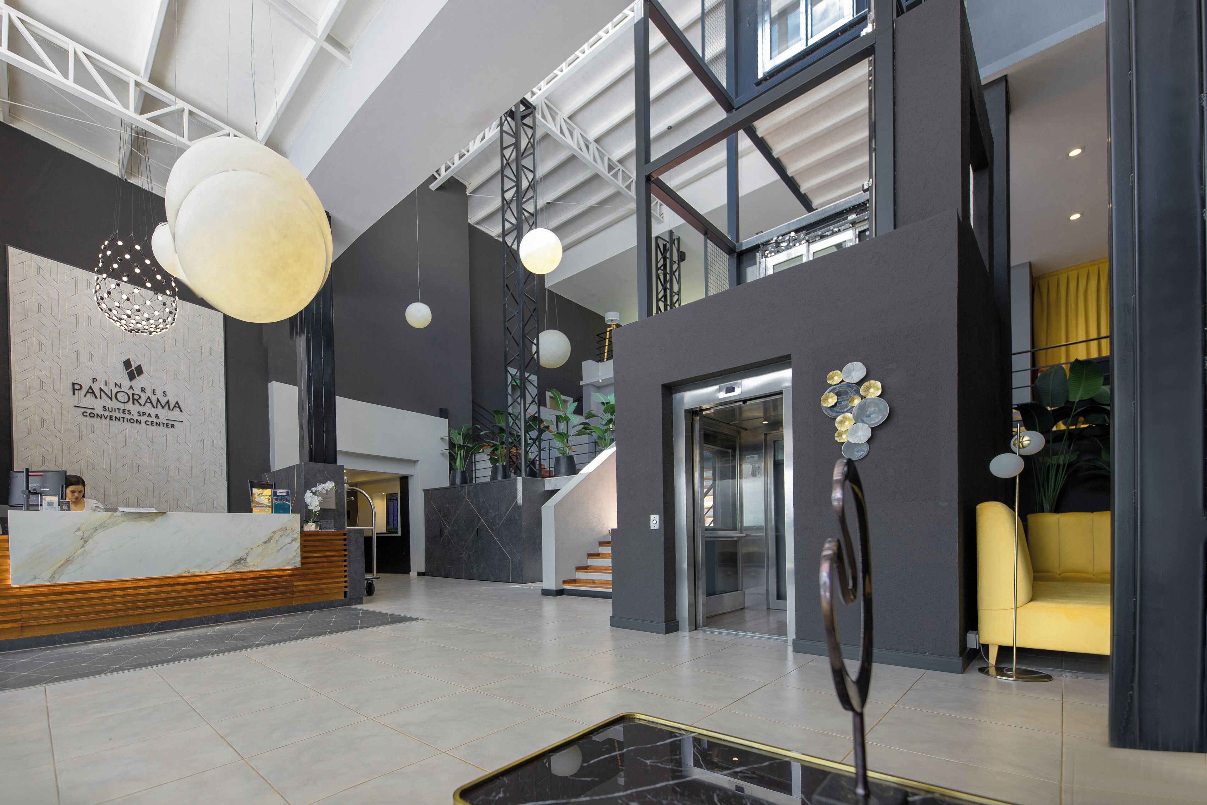 A modern hotel lobby with a reception desk, a staircase, and a yellow armchair.