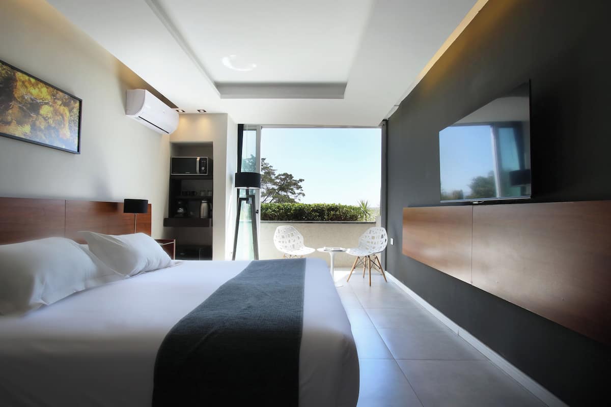 A modern hotel room with a large bed, a flat-screen TV, a coffee machine, and a balcony with a view.
