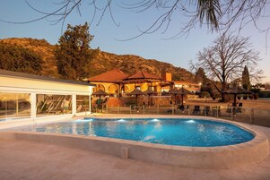 Una piscina con borde de piedra, un edificio con techo rojo y una colina al fondo.