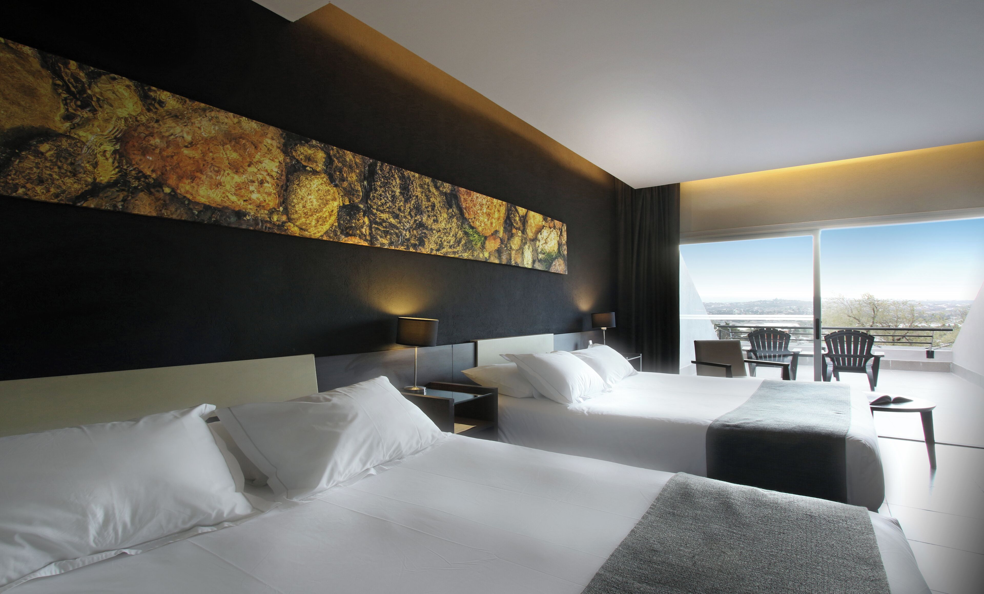 A modern hotel room with two beds, a large abstract painting on the wall, a balcony with a view, and a dining area.
