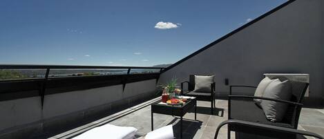 A rooftop terrace with a view of a lake and mountains, furnished with a table, chairs, and a towel.