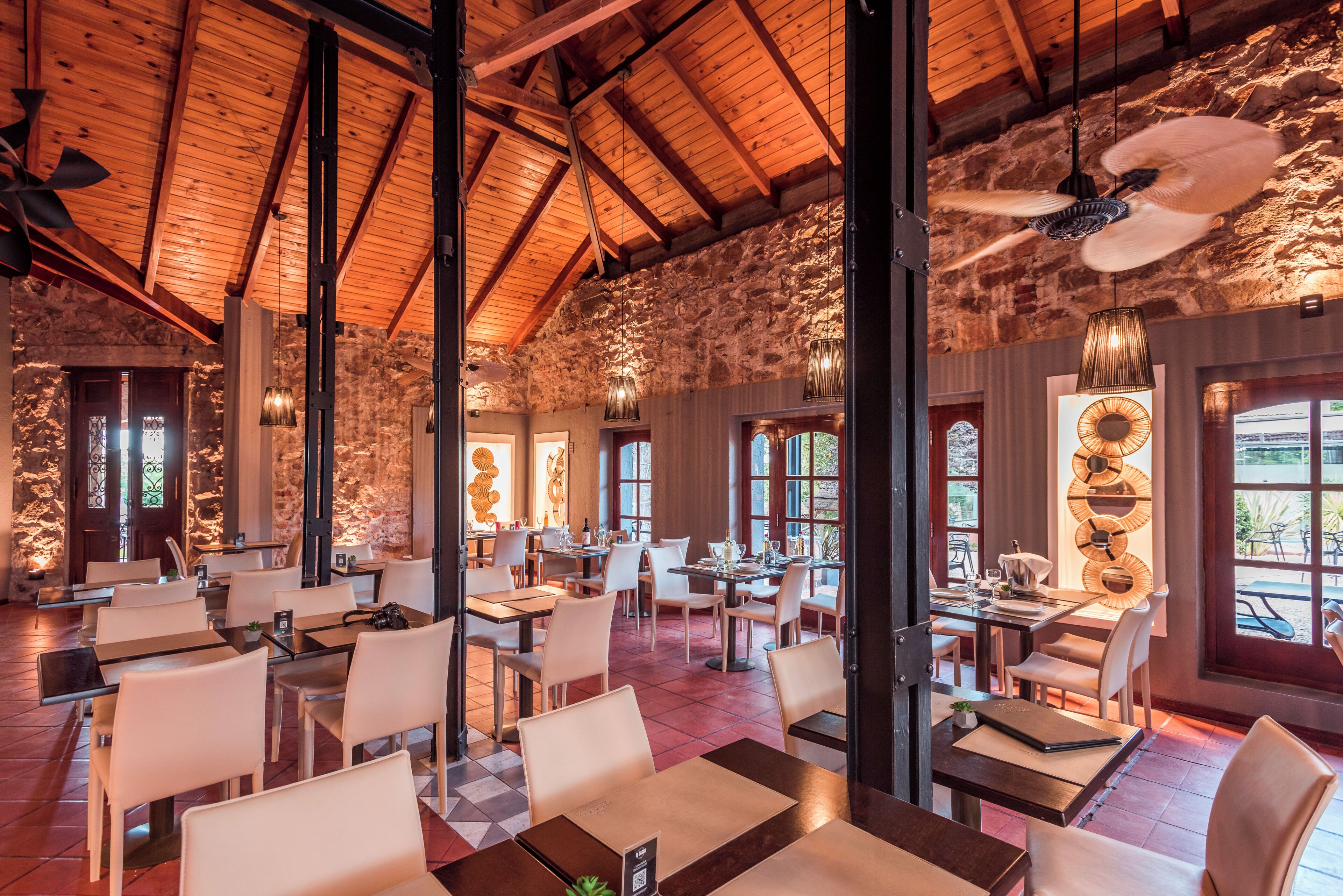 A spacious restaurant with high wooden ceilings and stone walls, featuring multiple dining tables and chairs.