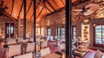 A spacious restaurant with high wooden ceilings and stone walls, featuring multiple dining tables and chairs.