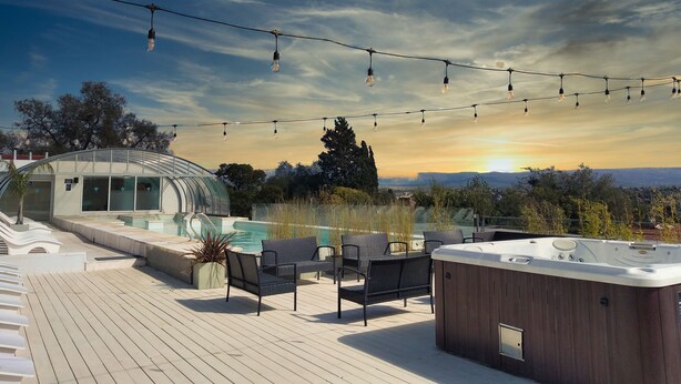 Een dak terras met een jacuzzi, lounge stoelen en een glazen kasconstructie.