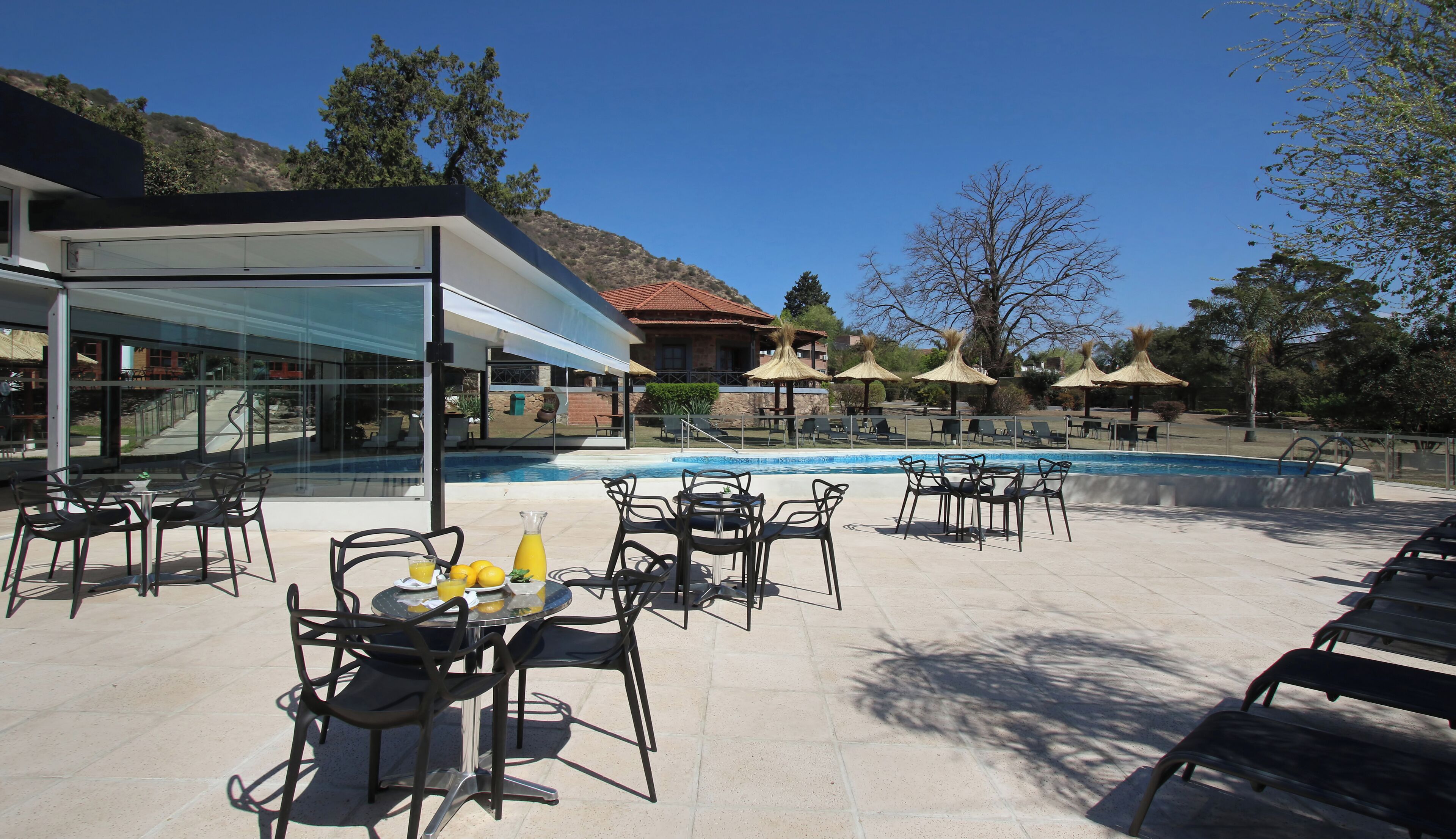 Un área junto a la piscina con mobiliario exterior y una estructura de cristal.