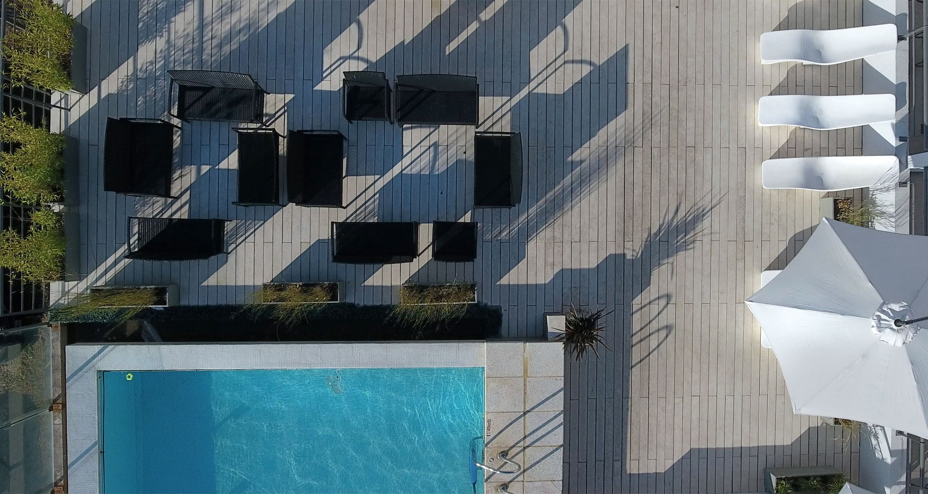 Un área de piscina en la azotea con múltiples sillas de descanso y sombrillas, rodeada por una terraza de madera.