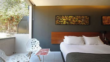 Una habitación de hotel con una cama, una silla, una mesa y obras de arte en la pared.