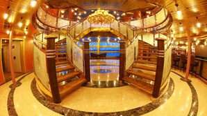 Una imponente escalera circular con candelabro, suelo de mármol y una zona de bar al fondo.