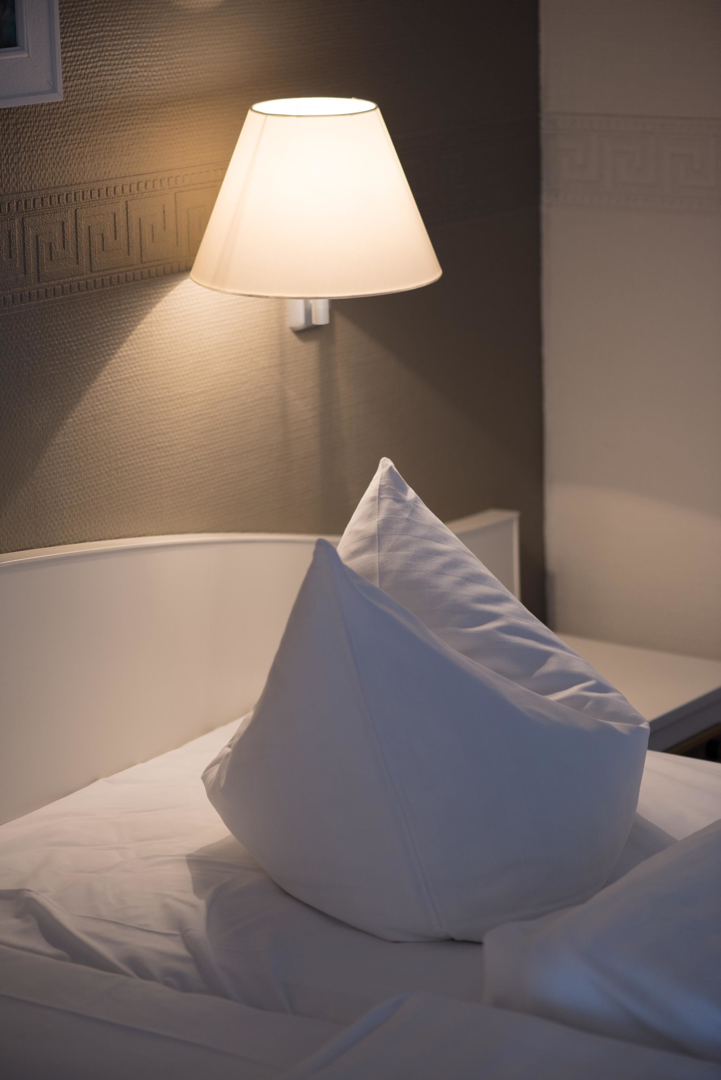A neatly made bed with a white pillow and a wall-mounted lamp providing soft lighting.