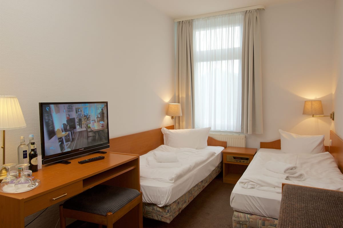 Une chambre d’hôtel avec un lit, un bureau équipé d’un ordinateur, une télévision et une fenêtre avec des rideaux.