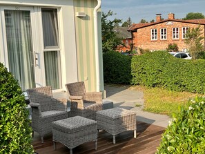 A patio with wicker furniture, a sliding glass door, and a brick house in the background. - Panorama Hotel Lohme (Lohme)