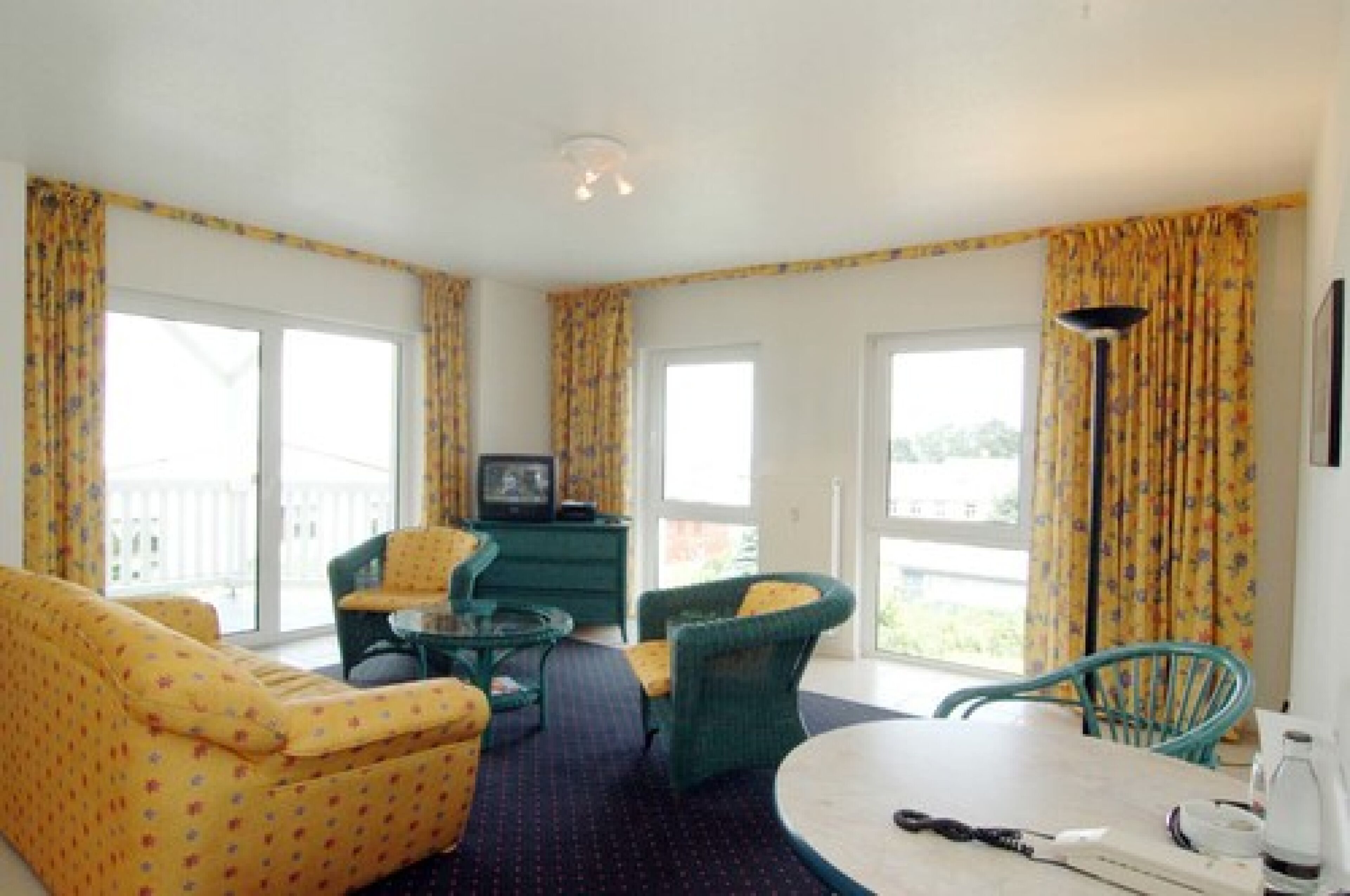 A room with a sofa, two chairs, a small table, a television, and a lamp.