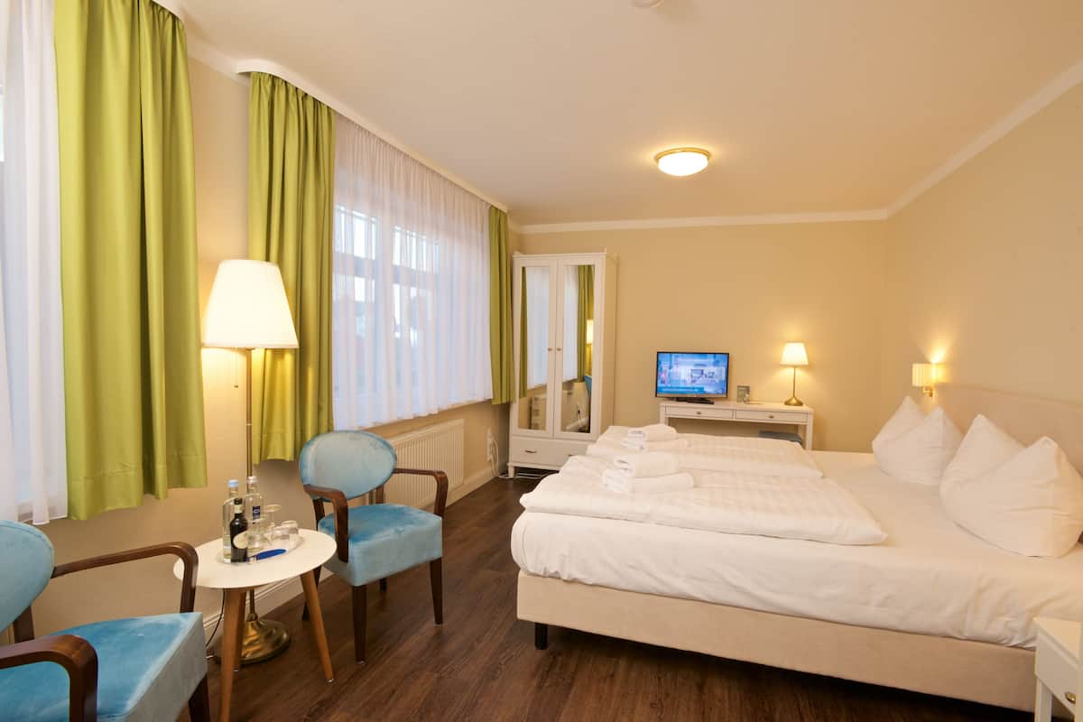 Une chambre d’hôtel avec un lit, deux chaises, une petite table avec une lampe, une télévision et un miroir.