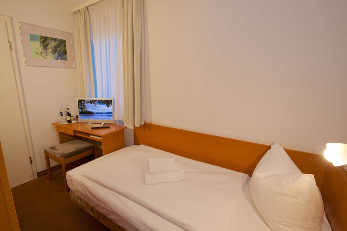 Une chambre d’hôtel avec un lit, un bureau avec un ordinateur, une chaise et une fenêtre avec des rideaux.