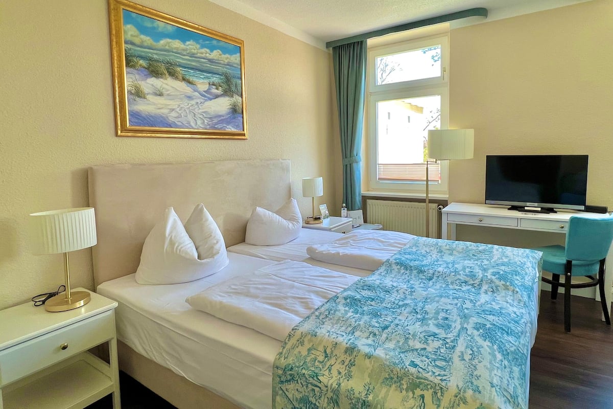 Une chambre d’hôtel avec un lit, un bureau avec une télévision, une chaise, une lampe et un tableau au mur.
