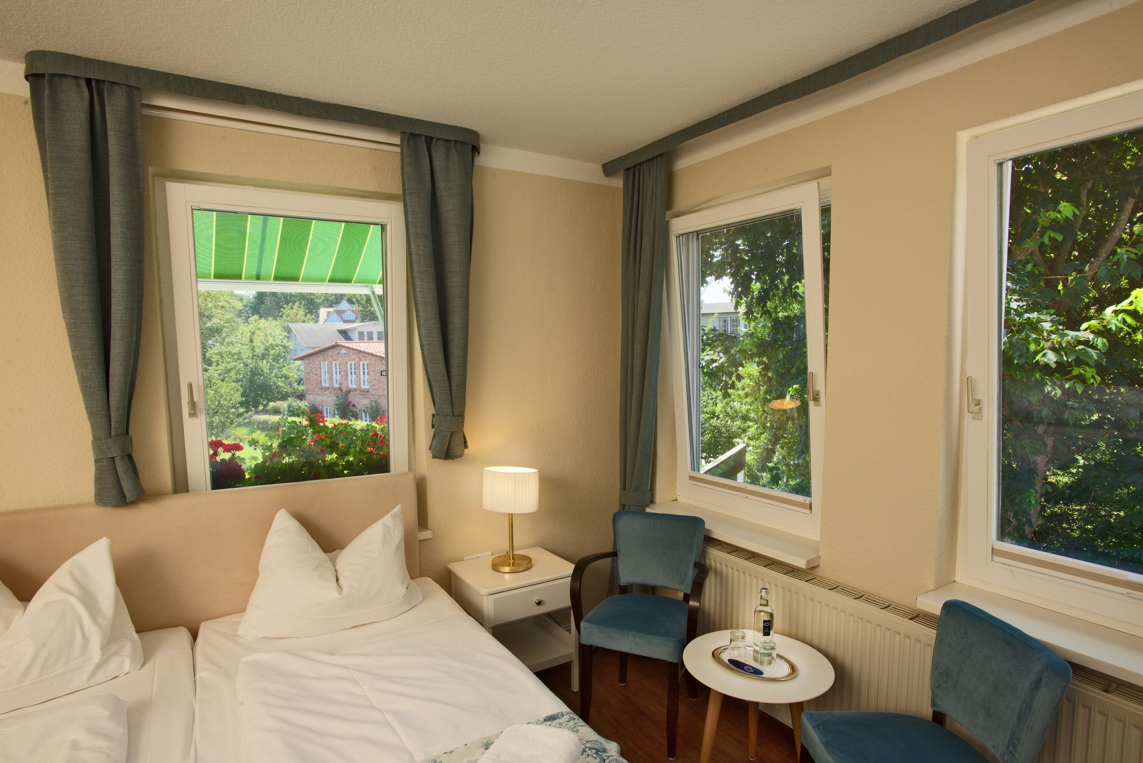 A hotel room with a bed, two chairs, a small table, and a window with curtains.