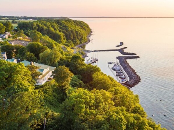 A coastal area with a dock and boats, surrounded by dense greenery and a few buildings. - Panorama Hotel Lohme (Lohme)