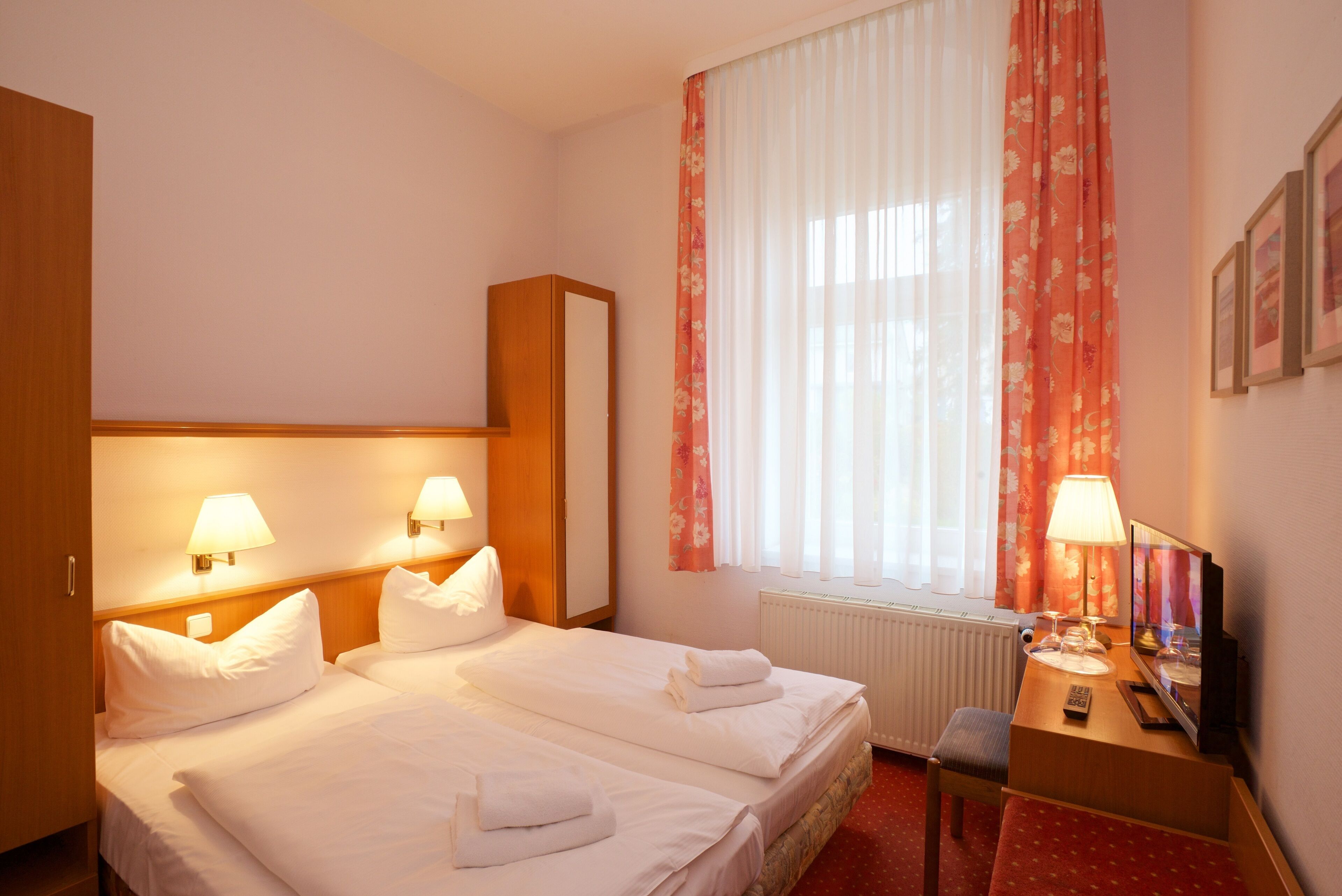 A hotel room with two beds, a desk with a chair, a TV, and a window with curtains.