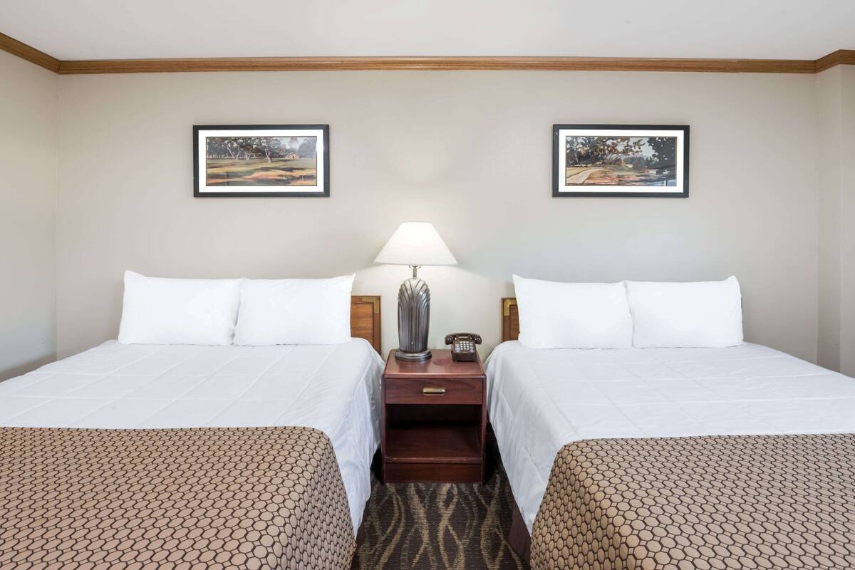 A hotel room with two beds, a nightstand with a lamp, and framed pictures on the wall.