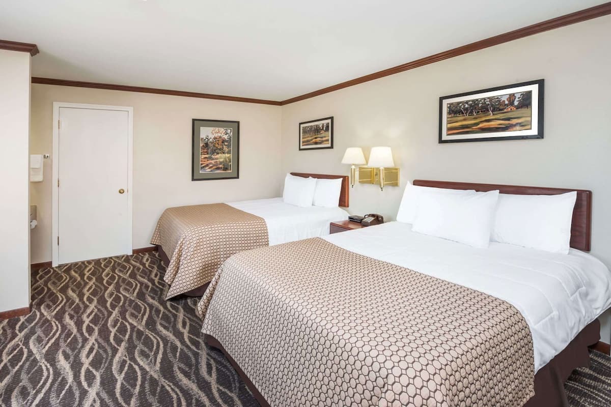A hotel room with two beds, a door, a wall-mounted lamp, and two framed pictures.