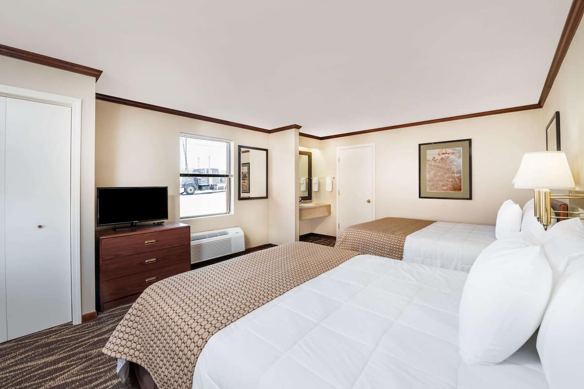 A hotel room with two beds, a TV, a dresser, and a window with a city view.