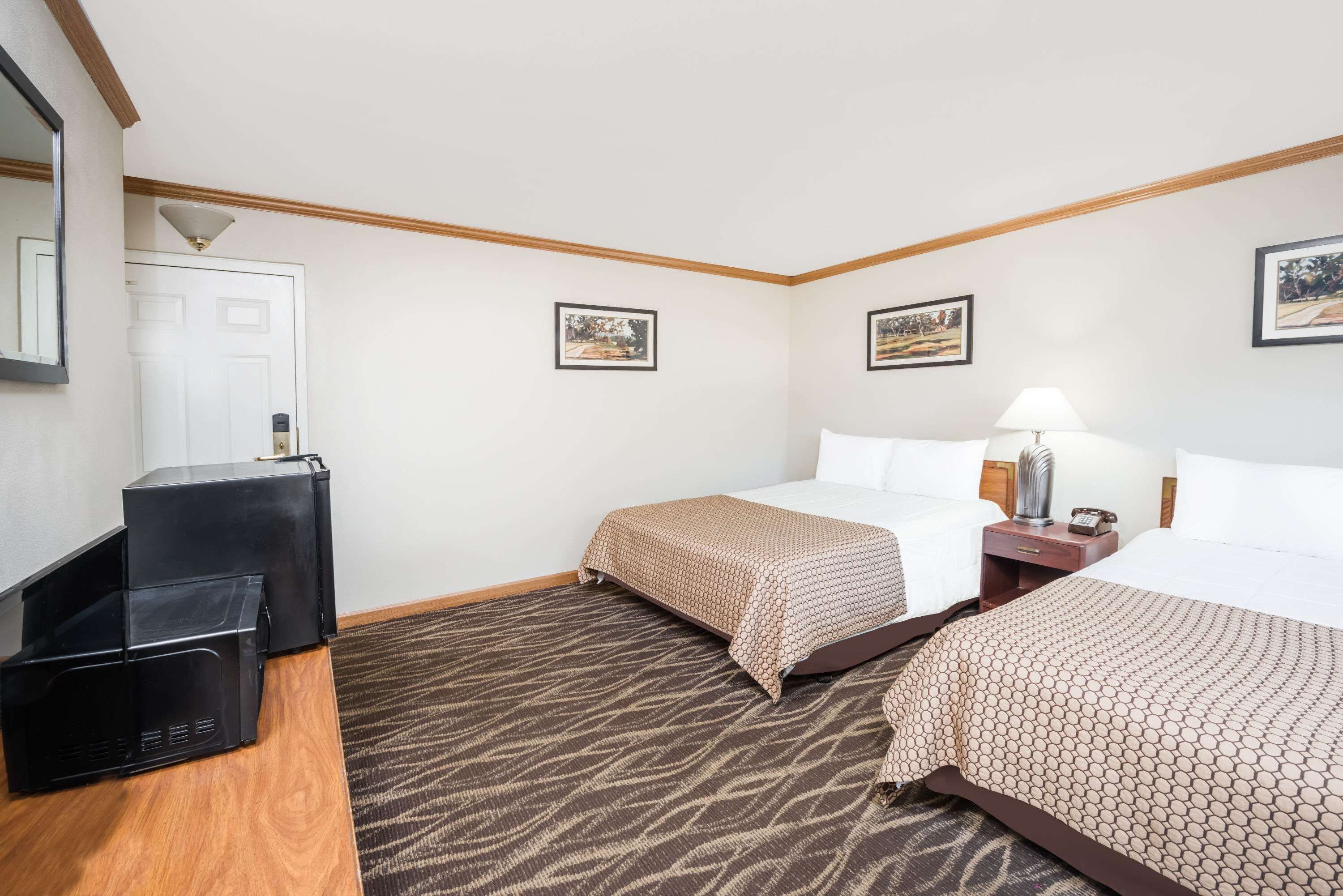 A hotel room with two beds, a desk, a chair, a lamp, and a door.