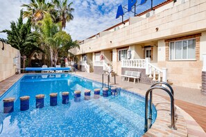 Una piscina con cubierta de baldosas, rodeada de palmeras y un edificio con un letrero que dice "AP".