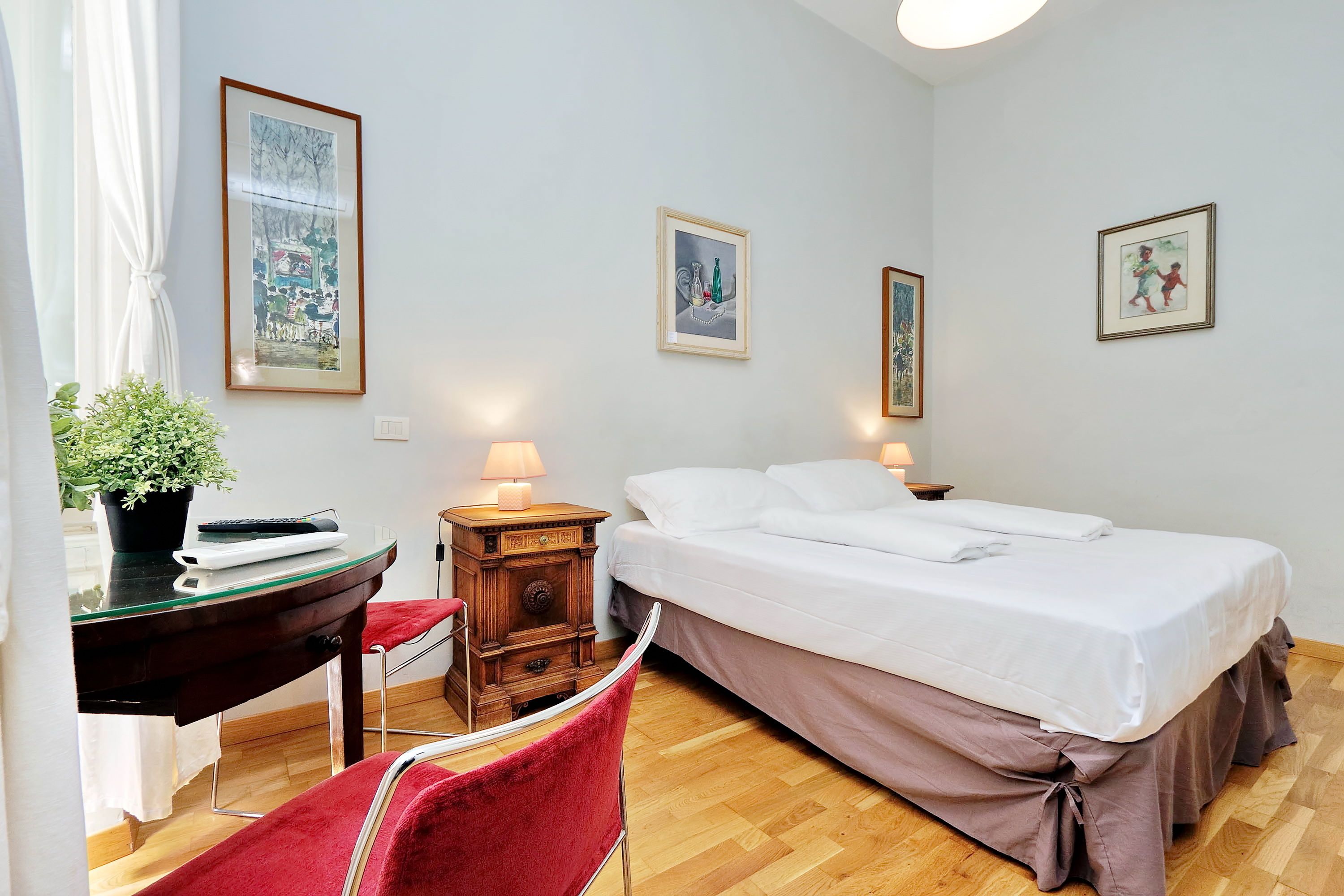 Een hotelkamer met een bed, nachtkastje, lamp, stoel, bureau en een pot met een plant.