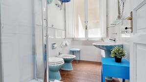 Casa de banho com cabine de chuveiro em vidro, lavatório branco, sanita azul e toucador azul.