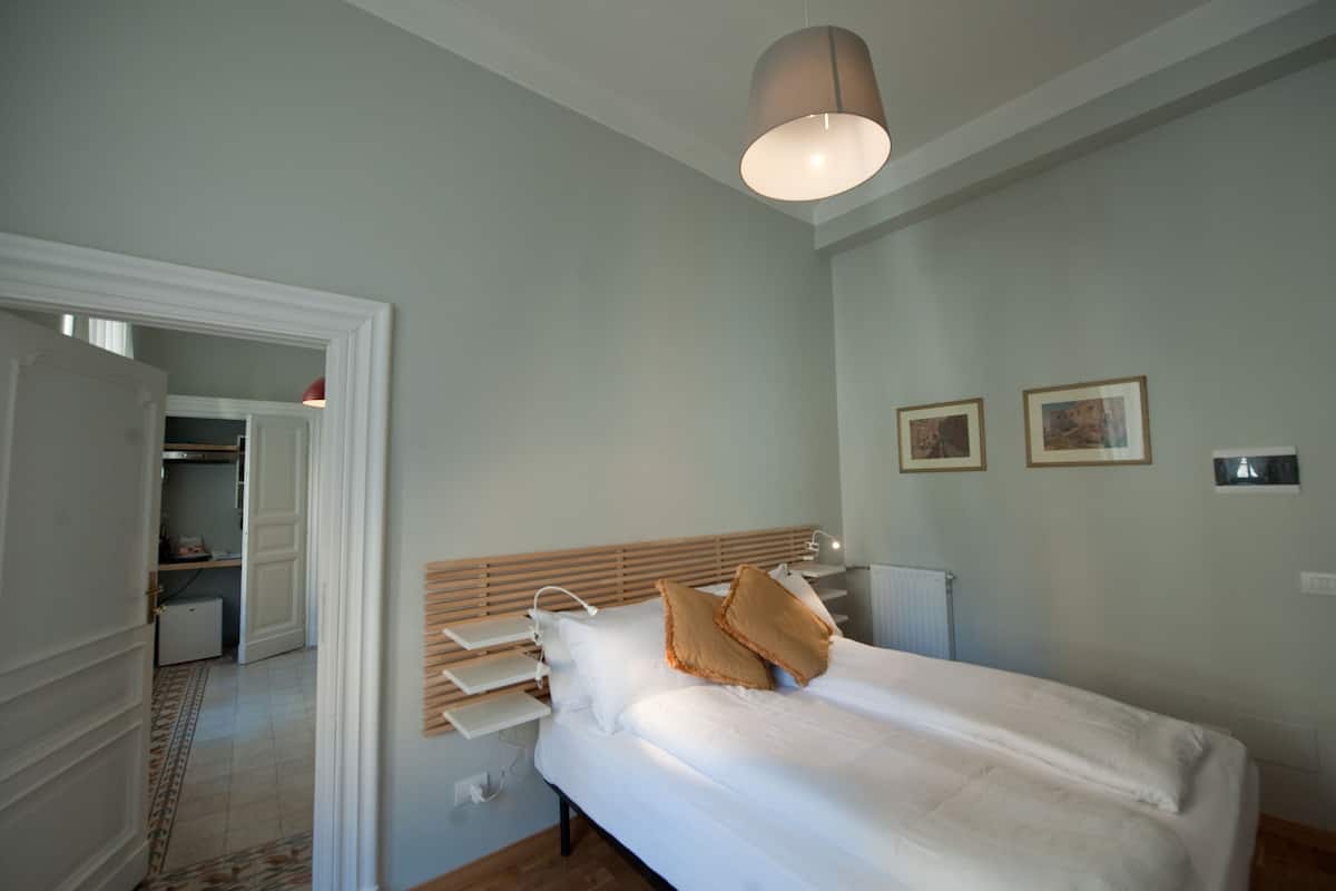 Un dormitorio con cama, mesitas de noche, una lámpara en el techo y una puerta que da a un baño.