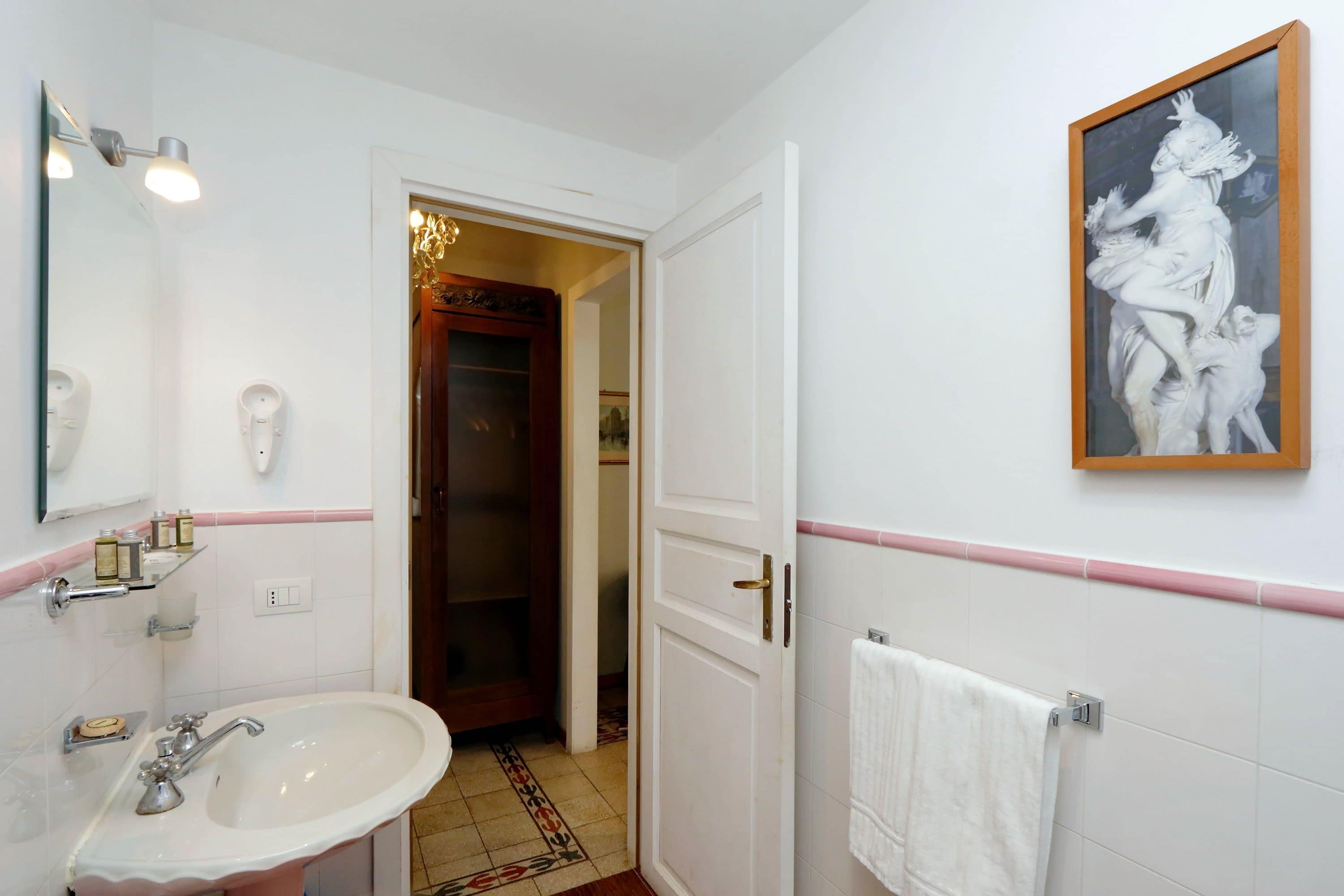 A bathroom with a white sink, mirror, and a framed artwork on the wall.