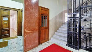 Um corredor com piso de mármore e um tapete vermelho que conduz a uma porta de madeira e uma escada com corrimão de metal.