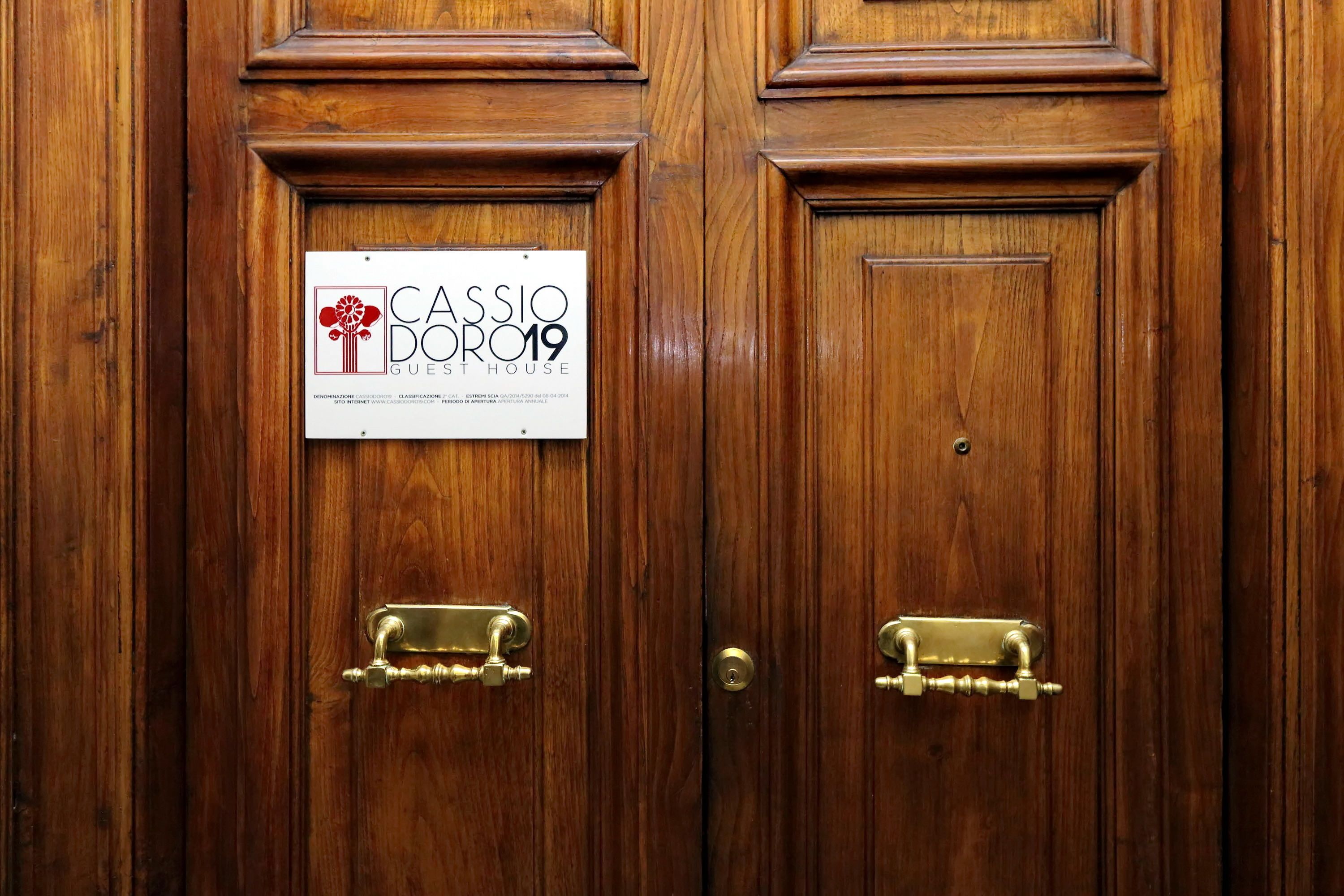 A wooden door with a brass handle and a sign that reads "Cassio Dorio 2019 Guest House".