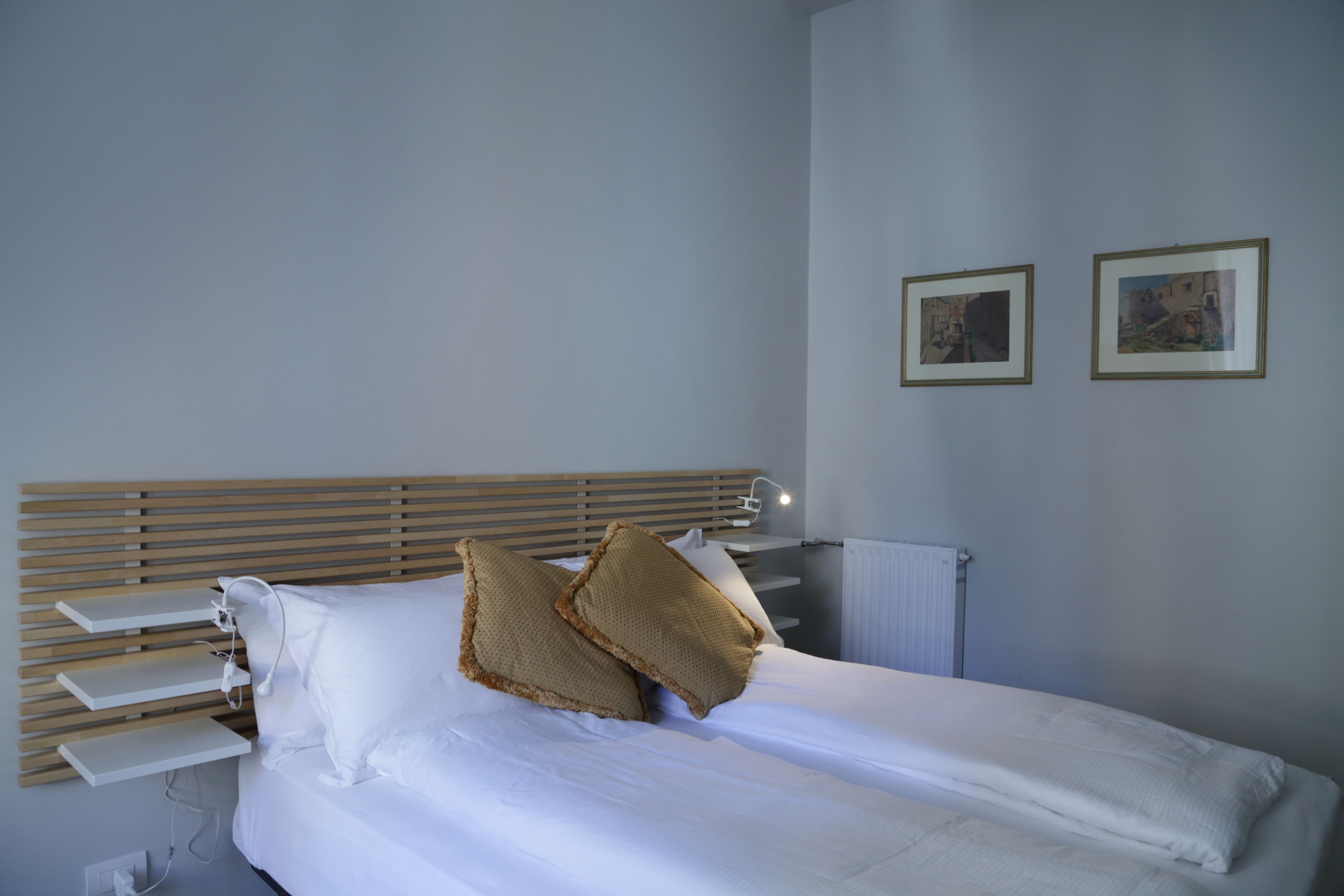A neatly made bed with white linens and two decorative pillows, a wooden headboard, and two framed pictures on the wall.