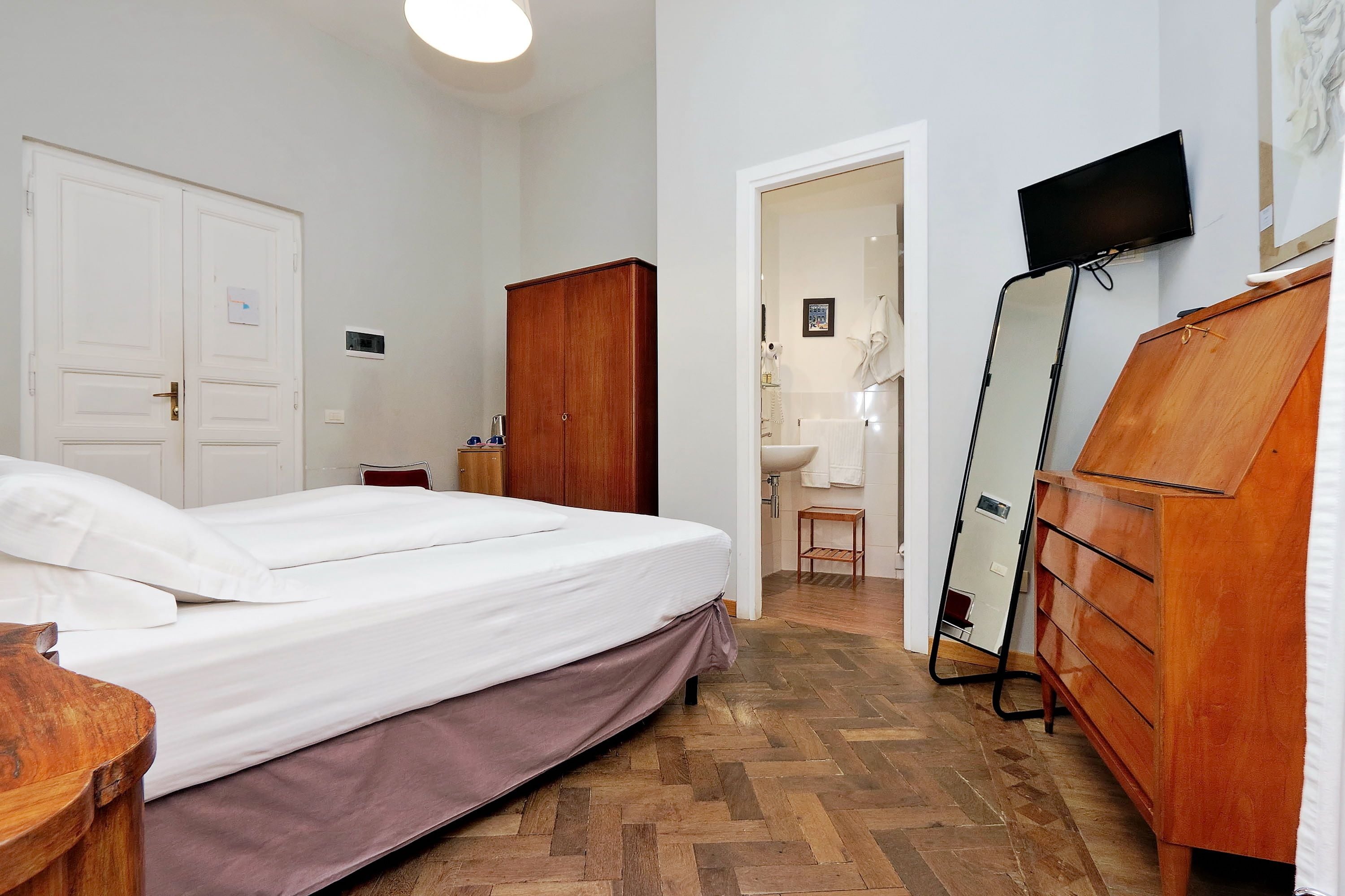 A bedroom with a bed, wooden wardrobe, and a television on the wall.