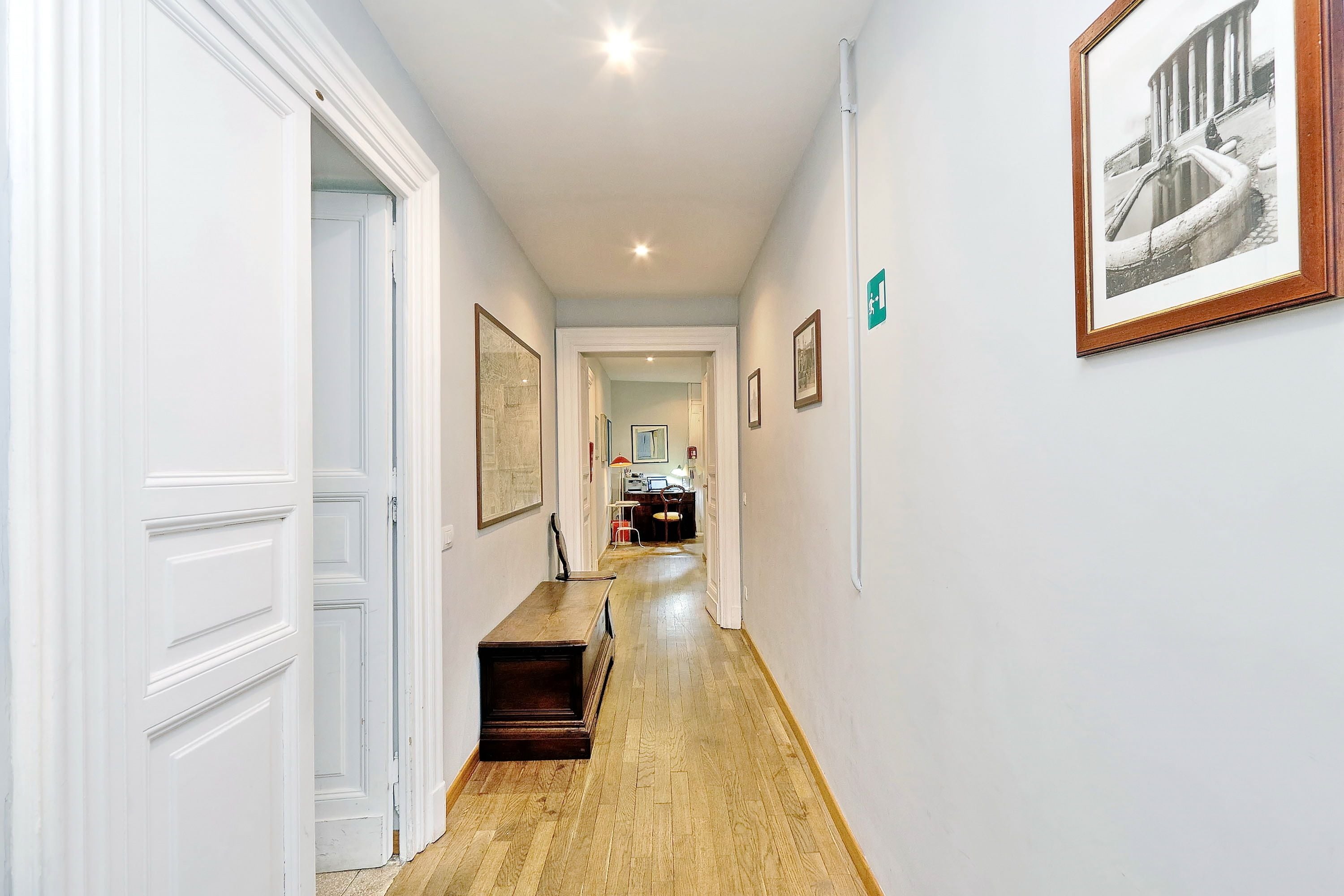 A hallway with white walls, wooden flooring, and framed pictures.