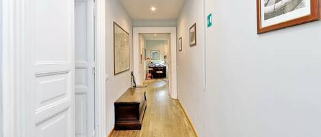 A hallway with white walls, wooden flooring, and framed pictures.