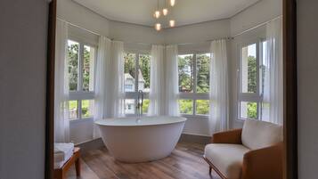 A modern bathroom with a freestanding bathtub, large windows, and a wooden floor.
