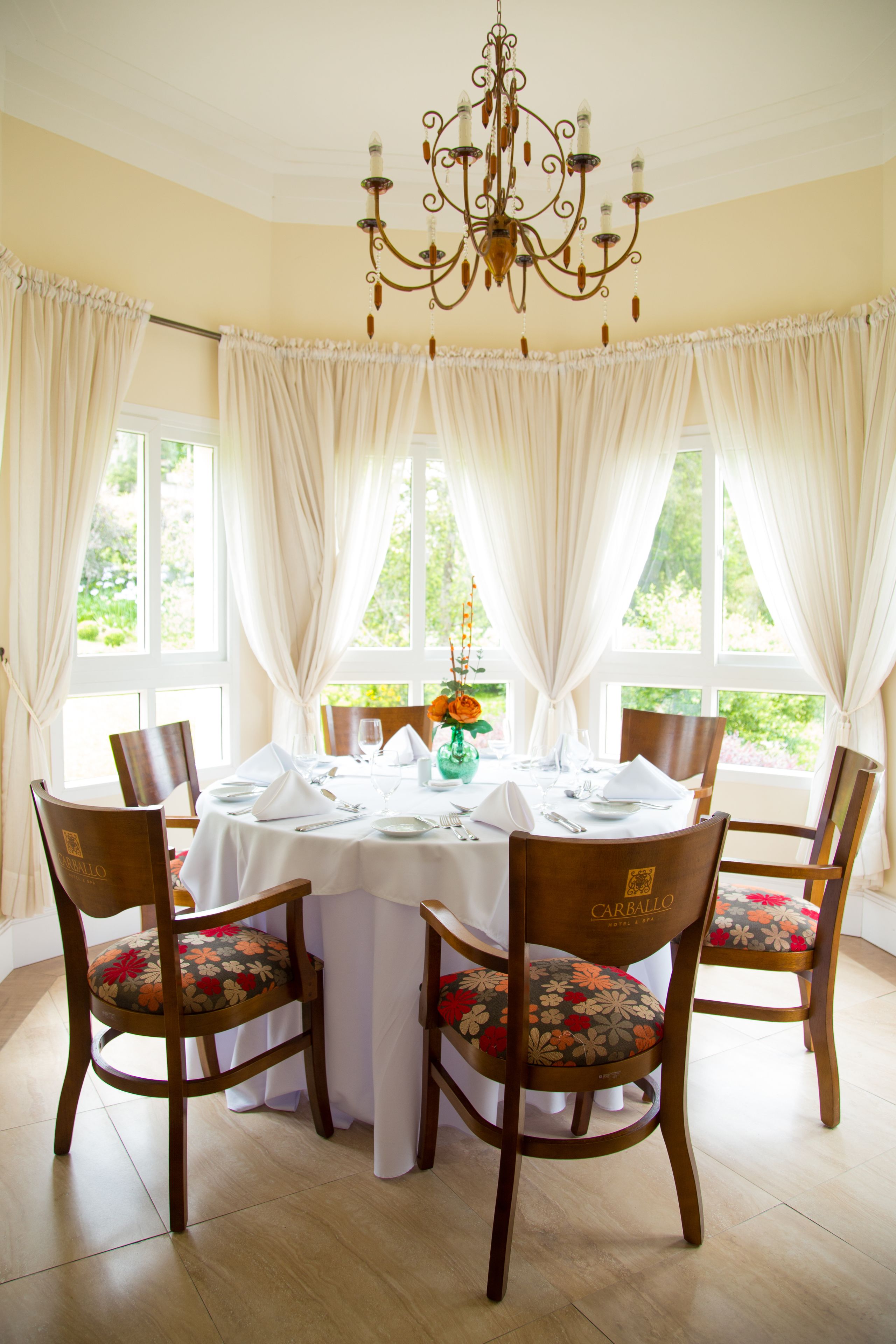 A dining room with a round table set for six, surrounded by six chairs with floral upholstery.