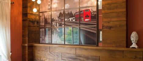 A seating area with leather chairs and a round table, a large framed picture of a red bus on a bridge, and wooden paneling on the wall.