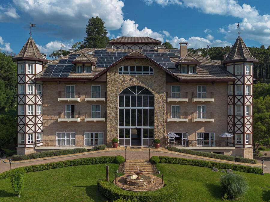 A large, historic building with a central arched entrance, multiple balconies, and solar panels on the roof.