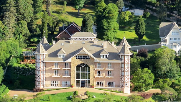 A large, multi-story building with a prominent central entrance, surrounded by lush greenery and other residential structures.