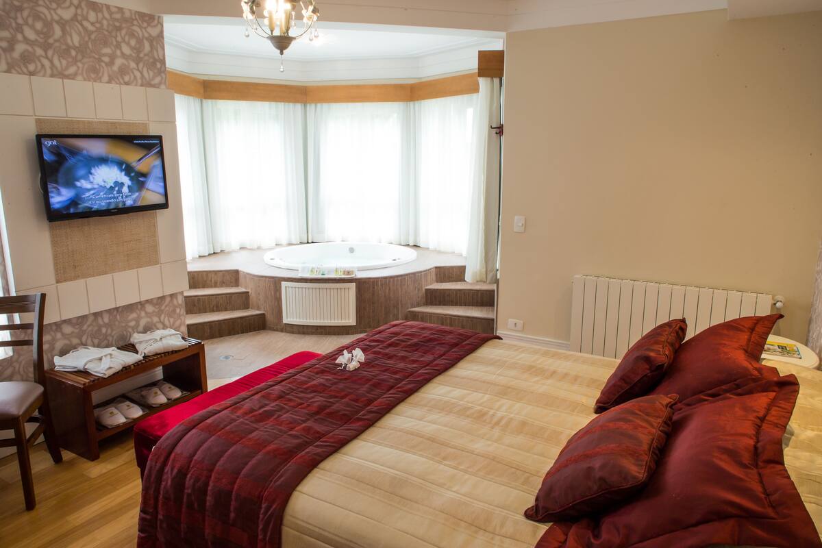 Quarto de hotel com uma cama grande, televisão na parede, banheira e vista para o exterior.