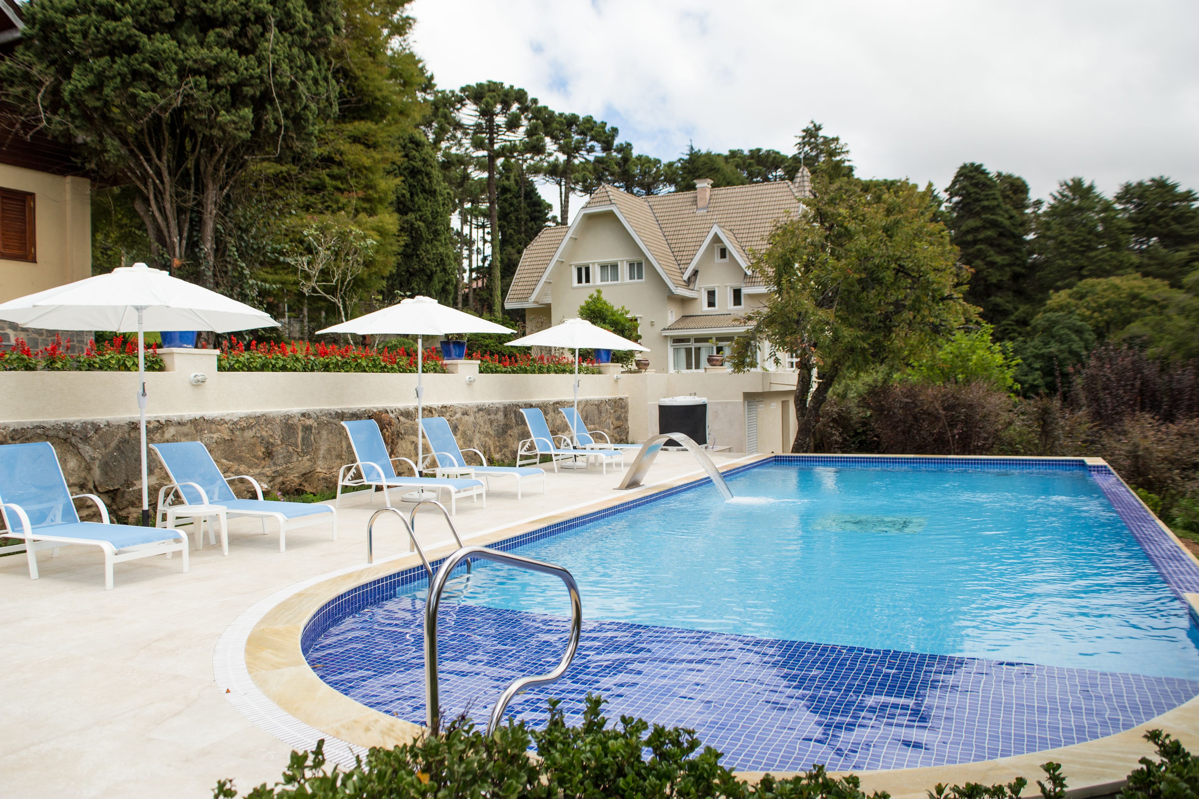 A swimming pool with blue-tiled edges, surrounded by lounge chairs and white umbrellas.