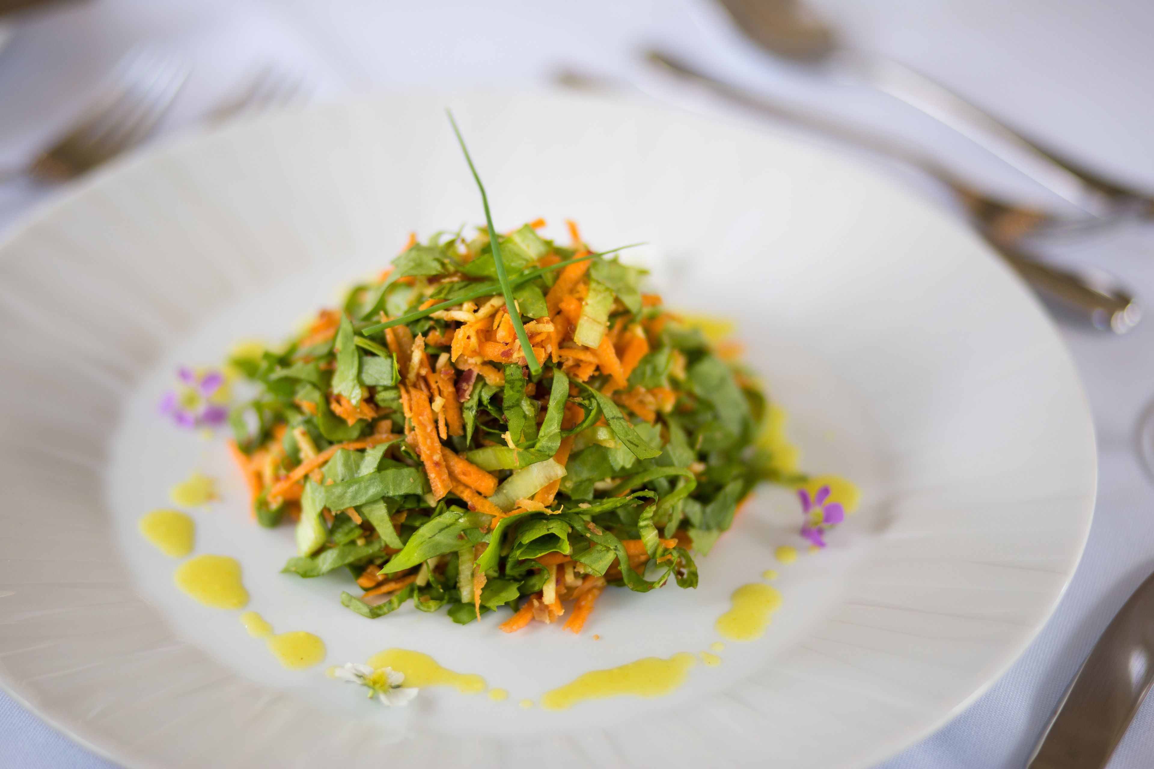 A white plate with a salad, a fork, and a knife on a tablecloth.