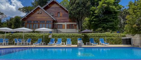 Una piscina con bordes de azulejos azules, rodeada de sillas de descanso y sombrillas.