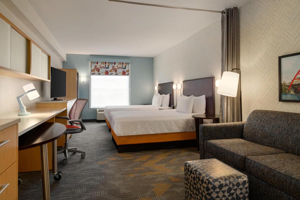 A hotel room with a bed, a desk with a computer, a chair, a sofa, and a lamp.