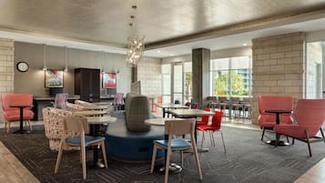 A modern indoor space with round tables and chairs, a central seating area, and large windows providing natural light.