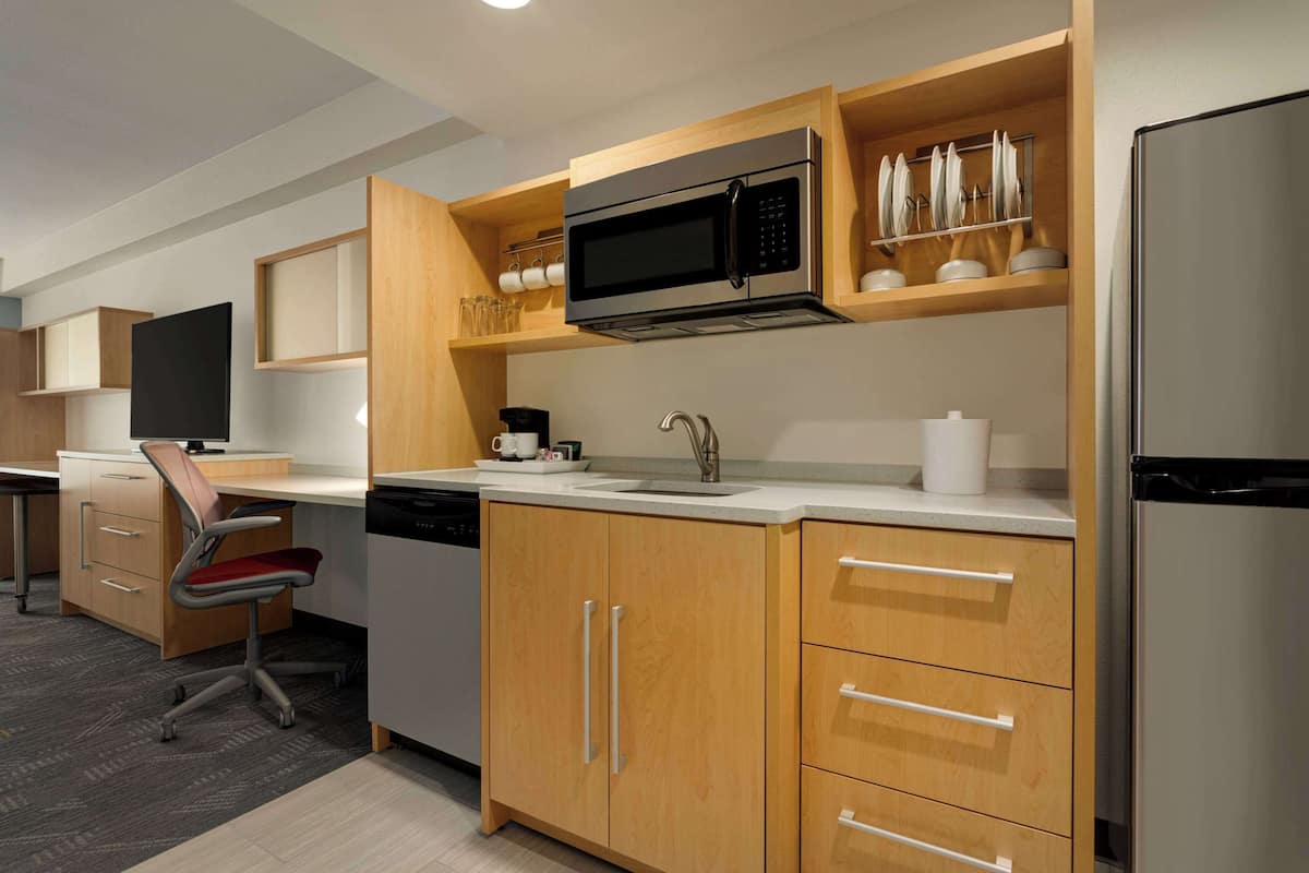 A compact kitchen with wooden cabinets, a stainless steel microwave, a sink, and a dishwasher.
